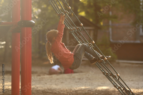 young blonde girl relaxing on a climbing net of a playground in a schoolyard in bright sunny light photo