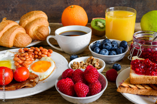 Breakfast including coffee, fried egg ,bacon, beans, croissant, orange juice with nuts, fruits and berries.