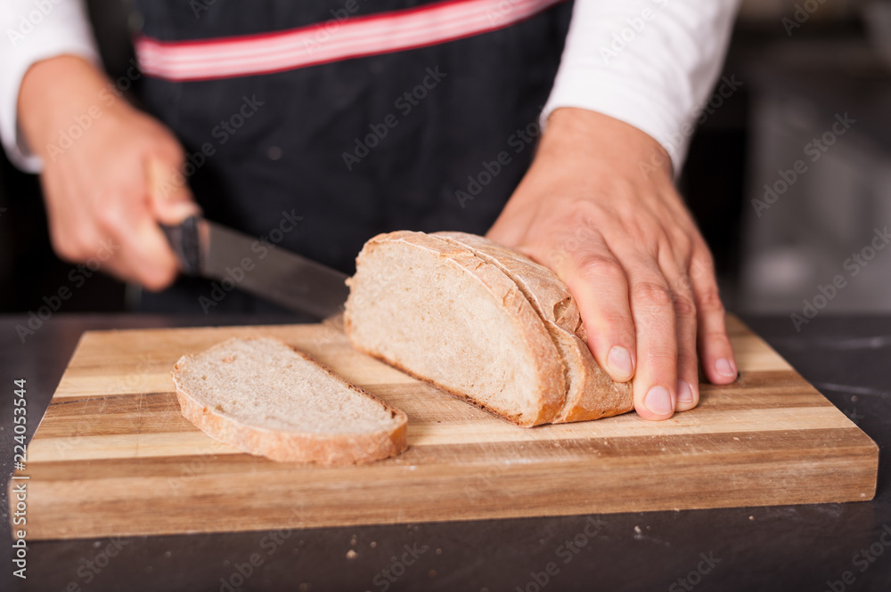 A man is cutting a sourdough loaf of bread on wooden board.