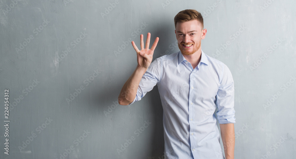 Young redhead business man over grey grunge wall showing and pointing up with fingers number four while smiling confident and happy. Young redhead business man over grey grunge wall showing and pointing up with fingers number four while smiling confident and happy.
