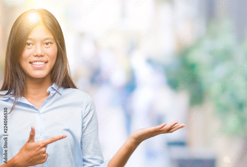 Young asian business woman over isolated background amazed and smiling to the camera while presenting with hand and pointing with finger.