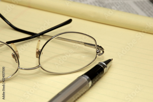A yellow lined legal pad, reading glasses and a ballpoint pen in an office.