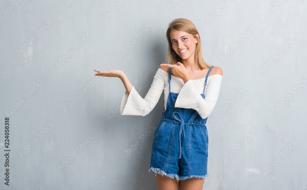 Beautiful young woman standing over grunge grey wall amazed and smiling to the camera while presenting with hand and pointing with finger. Beautiful young woman standing over grunge grey wall amazed and smiling to the camera while presenting with hand and pointing with finger.