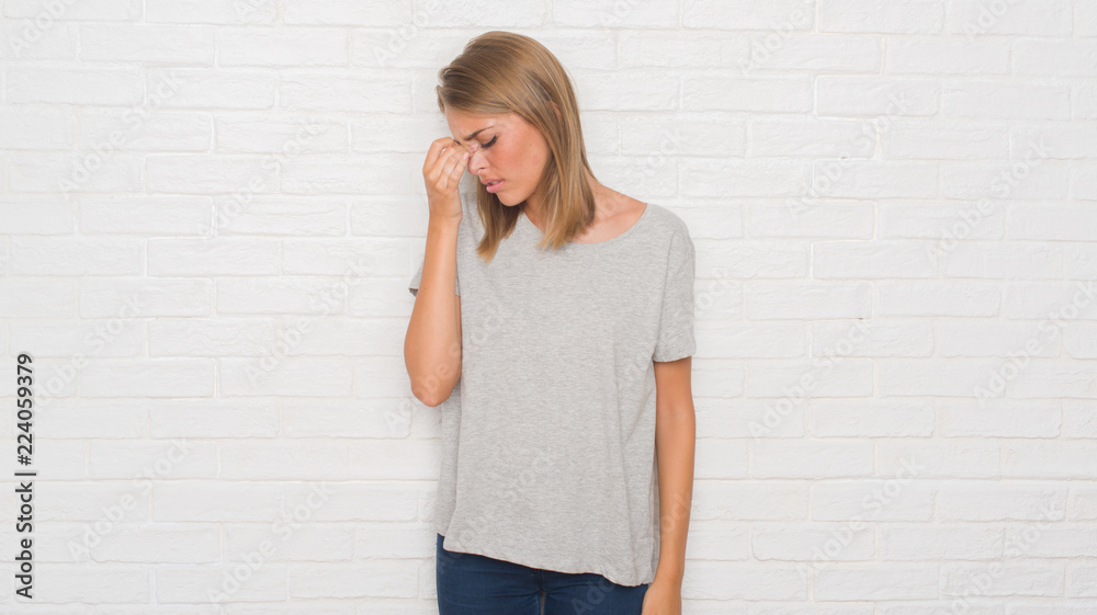 Beautiful young woman over white brick wall tired rubbing nose and eyes feeling fatigue and headache. Stress and frustration concept. Beautiful young woman over white brick wall tired rubbing nose and eyes feeling fatigue and headache. Stress and frustration concept.