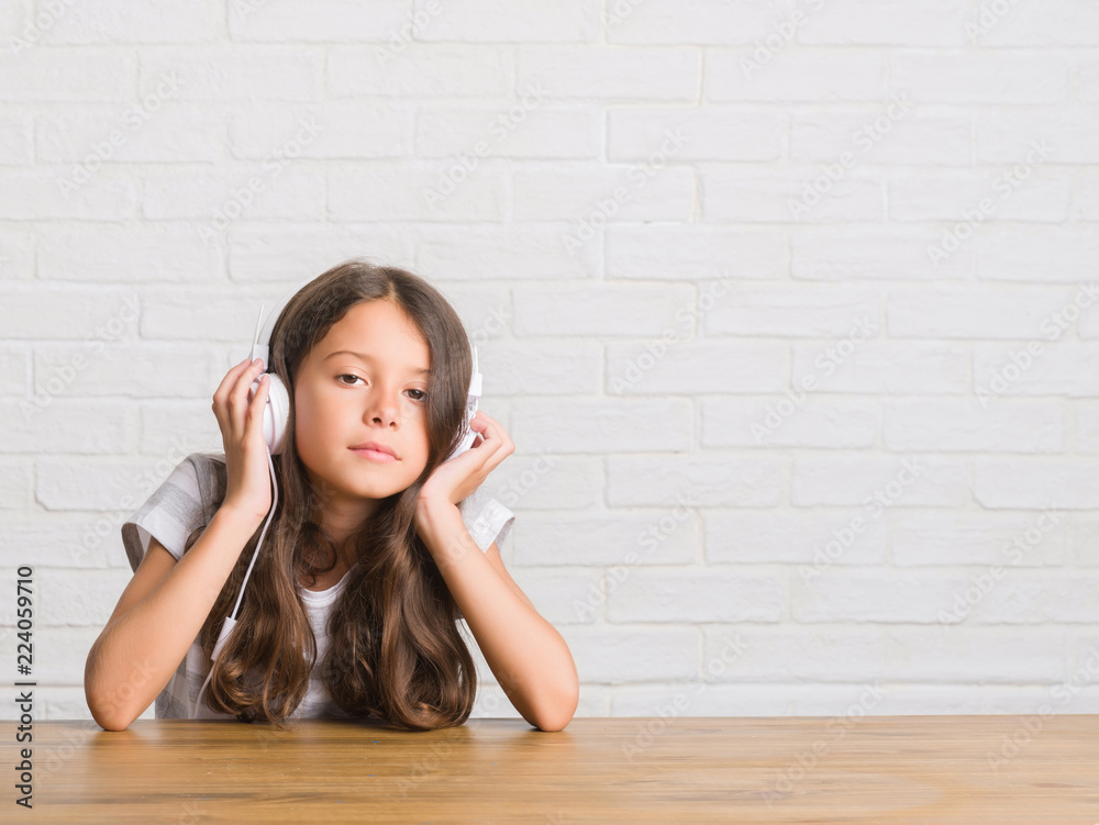 Young hispanic kid sitting on the table wearing headphones with a confident expression on smart face thinking serious Young hispanic kid sitting on the table wearing headphones with a confident expression on smart face thinking serious