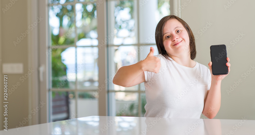 Down syndrome woman at home using smartphone happy with big smile doing ok sign, thumb up with fingers, excellent sign Down syndrome woman at home using smartphone happy with big smile doing ok sign, thumb up with fingers, excellent sign