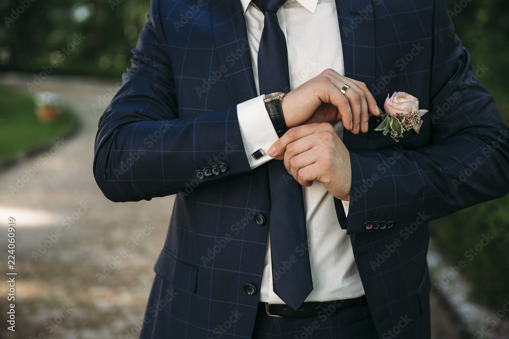 A man in a business suit, white shirt close-up of a cropped frame. The  businessman puts on cufflinks, wears a gold finger ring on his finger, an  expensive leather belt. Stock Photo