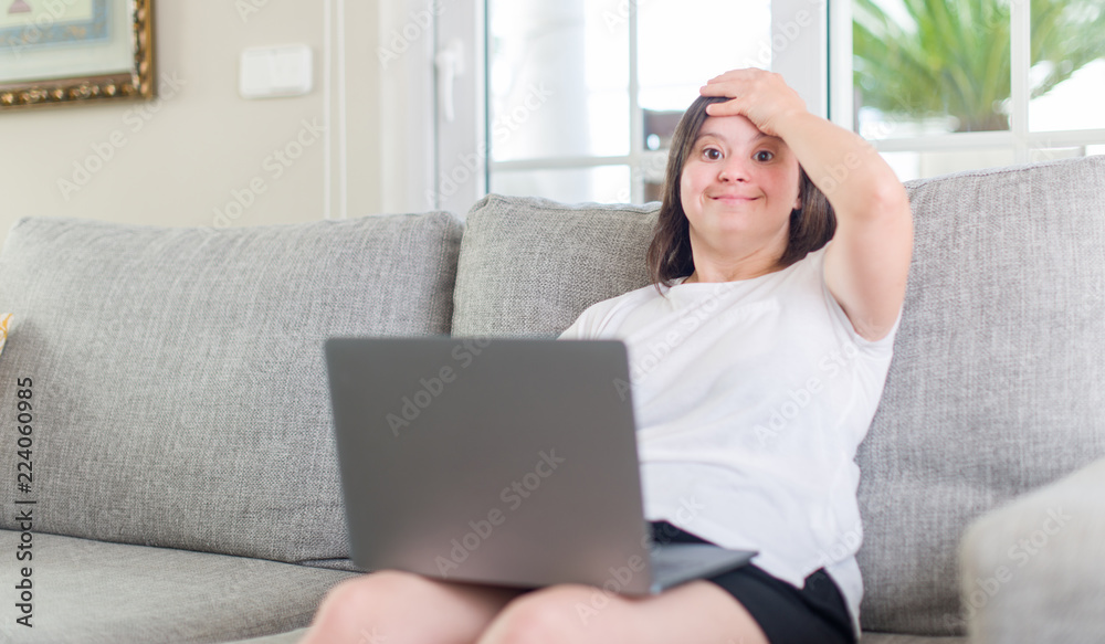 Down syndrome woman at home using computer laptop stressed with hand on head, shocked with shame and surprise face, angry and frustrated. Fear and upset for mistake. Down syndrome woman at home using computer laptop stressed with hand on head, shocked with shame and surprise face, angry and frustrated. Fear and upset for mistake.