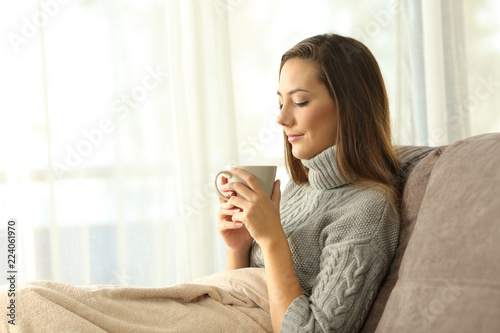 Pensive lady holding a cup of coffee at home in winter