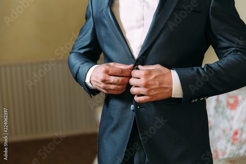 Close-up of a cropped frame of a business stylish man buttoning his jacket, standing in a stylish office with designer repair.