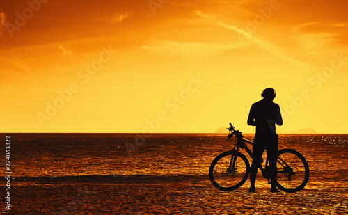 Cyclist with bike resting on beach at sunset © Daniel Ernst