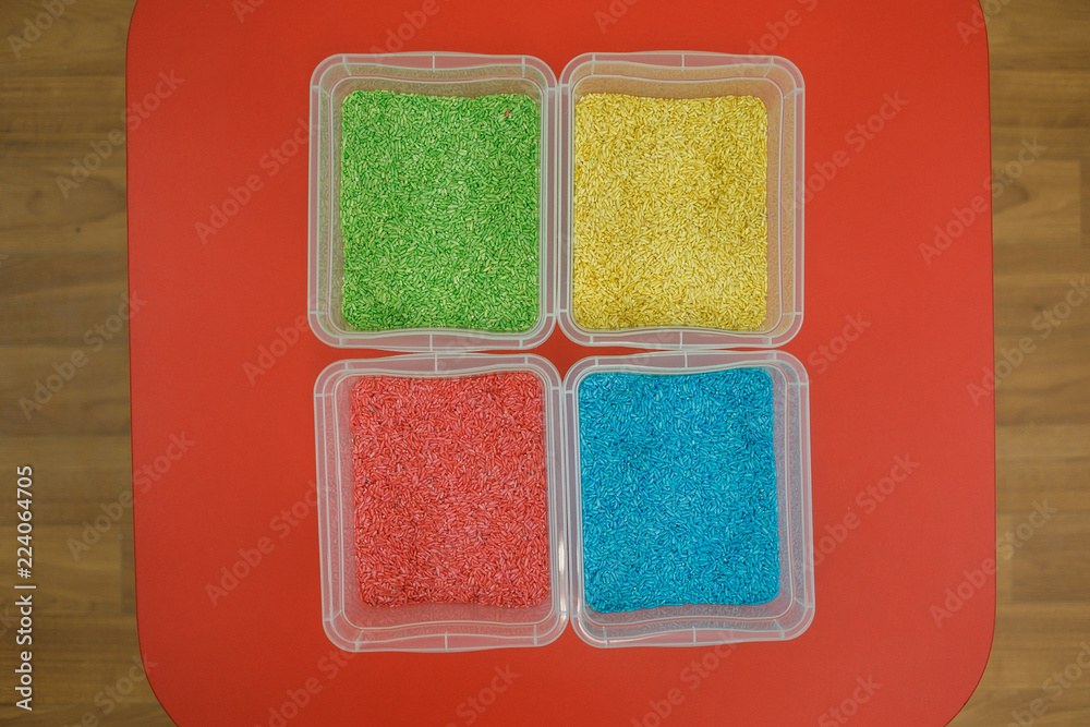 Fototapeta premium Rainbow sensory boxes for toddlers with colourful rice on red table. Universal educational kit in kindergarten.