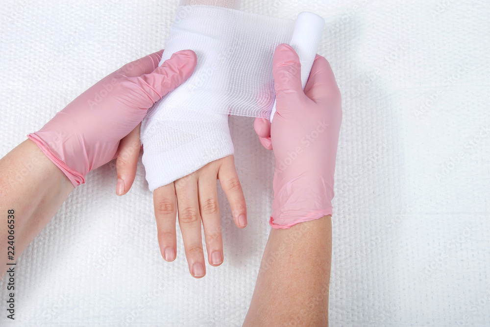 Young female hands wearing pink gloves wrapping gauze on young hand and