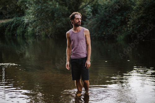 thoughtful and serious looking young man standing in a river