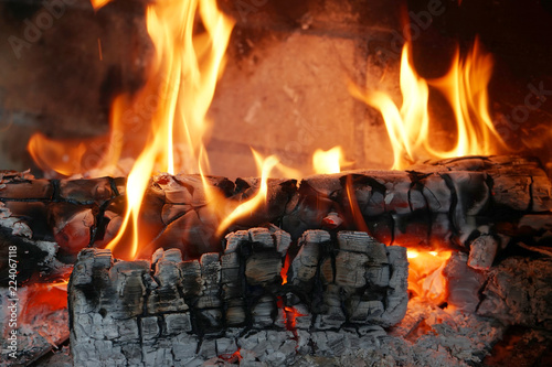 Burning firewood in the fireplace close-up. Close-up with burning logs and vivid burning orange and yellow flames. Flames crawl up the side of a piece of firewood in an open campfire.
