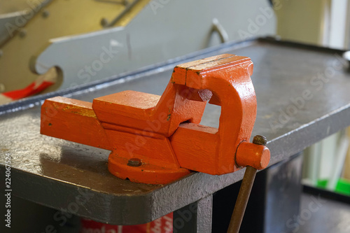 Wallpaper Mural Close-up orange clamp mounted grip with screw action grip and cast iron frame, in a machining workshop. Large Iron Vise on the Desktop in a farm. Torontodigital.ca