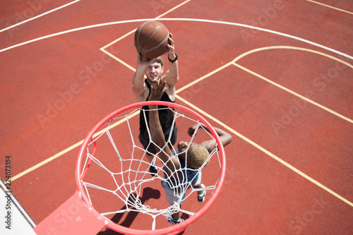 Above view portrait of young basketball player throwing ball in hoop on outdoor court lit by sunlight, copy space