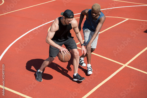 High angle action shot of two handsome muscular men playing basketball in outdoor court lit by sunlight, copy space
