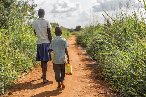 Two impoverished Ugandan kids carrying jerry cans on a walk to get water.