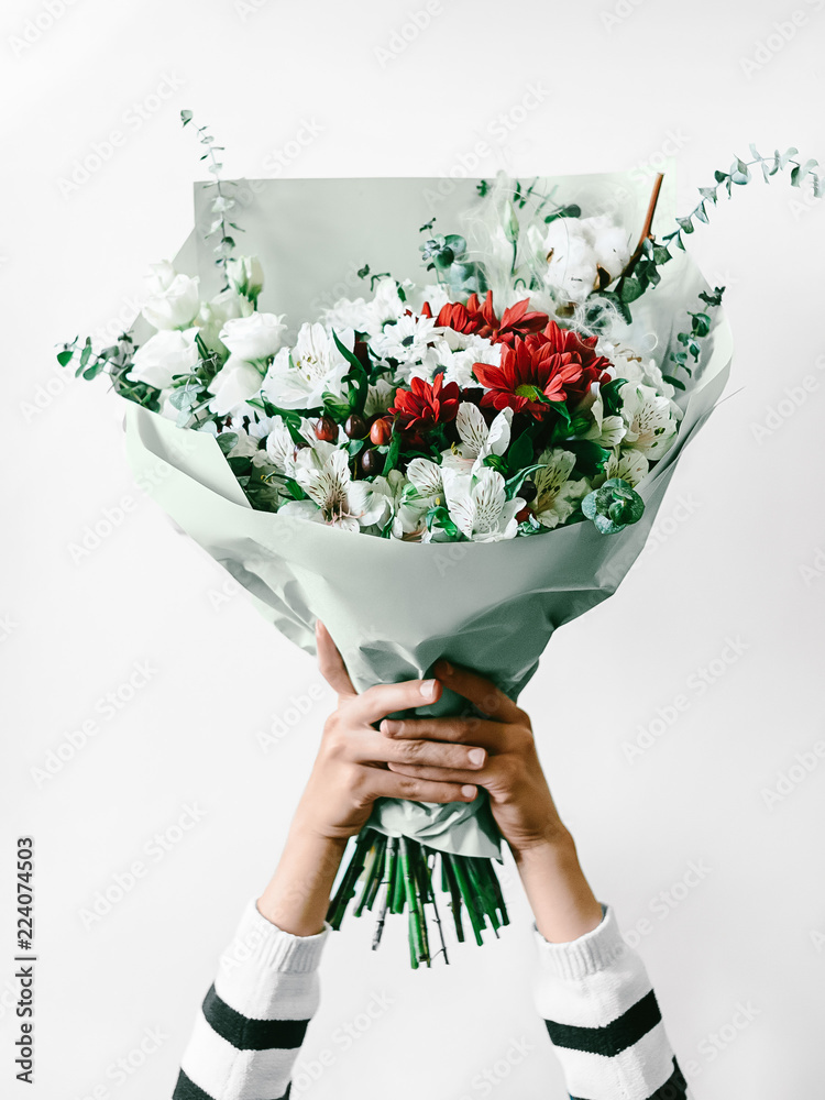 Flower arrangement against white background Close-up photo Woman is holding a large bouquet of flowers in a paper package in her hands