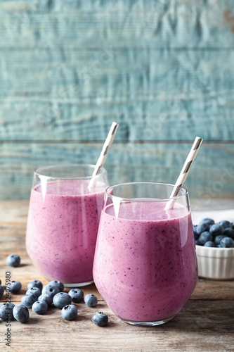 Tasty blueberry smoothie in glasses and berries on wooden table