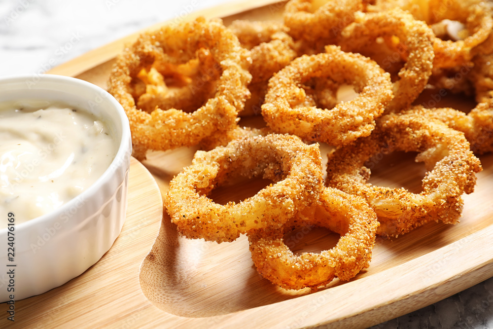 Homemade crunchy fried onion rings and sauce on wooden dish, closeup