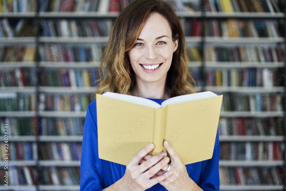 Portrait of woman in a library with opened book hold in hands, long hair. Young college student girl in co-working, concept of studying. Portrait of woman in a library with opened book hold in hands, long hair. Young college student girl in co-working, concept of studying.