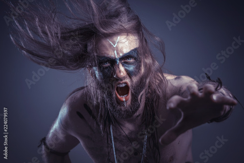 Dark tribal shaman or warlock summoning spirits using a deer skull and his ritual staff, halloween concept