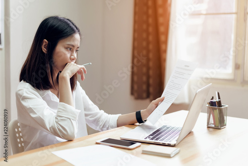 woman holding agreement documents and using laptop on table in office room, to plan advance budget..