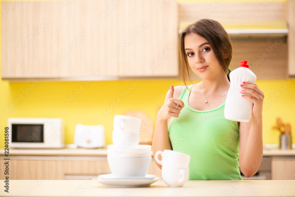 Young woman cleaning and washing dishes in kitchen