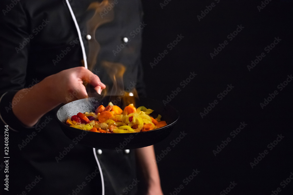 Professional chef and fire. Cooking vegetables and food over an open fire  on a dark background. Hotel service photo background. With copy space for  your text. Flambeau Stock Photo