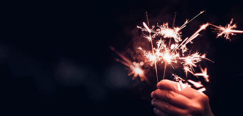 Hand holding burning Sparkler blast on a black bokeh background at night,holiday celebration event party,dark vintage tone