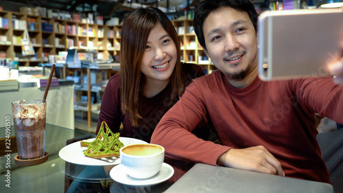 Asian couple taking the selfie with happiness action in modern coffee shop or workplace or co-working space or modern office  lifestyle and leisure concept