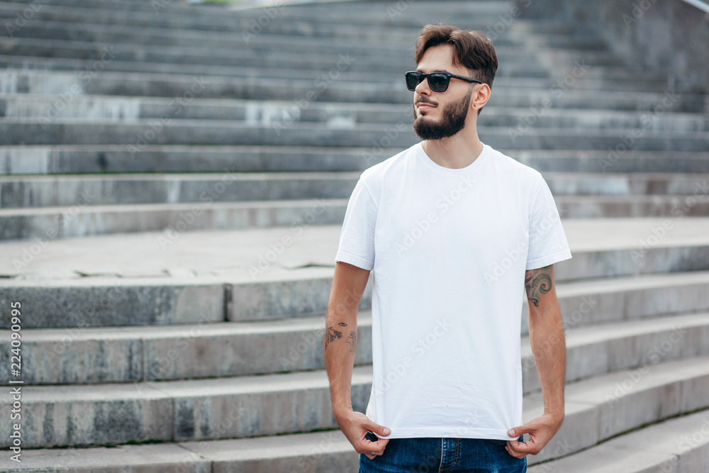 A young stylish man with a beard in a white T-shirt and glasses. Street photo A young stylish man with a beard in a white T-shirt and glasses. Street photo