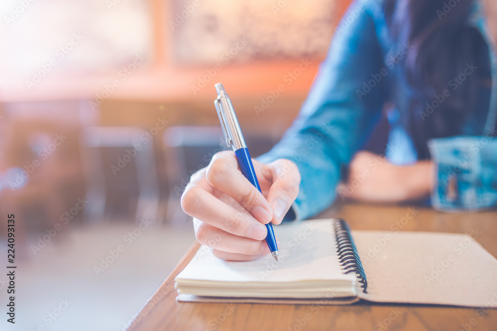 A woman's hand is writing in empty spiral notepad with a pen.
