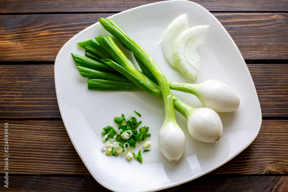 Three large Mexican onions which are green onions that have been allowed to grow bigger on a white plate with some smaller green onions sliced next to it on a kitchen table. Three large Mexican onions which are green onions that have been allowed to grow bigger on a white plate with some smaller green onions sliced next to it on a kitchen table.