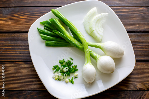 Three large Mexican onions which are green onions that have been allowed to grow bigger on a white plate with some smaller green onions sliced next to it on a kitchen table.