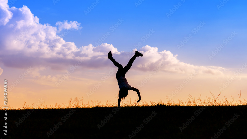 Silhouette happy child playing upside down outdoors in summer park walking on hands at sunset
