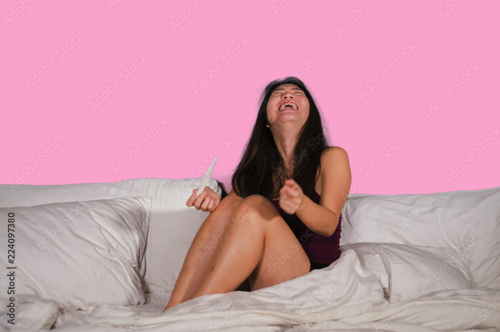 young happy and excited Asian Chinese woman in bed holding pregnancy test checking surprised positive pregnant result smiling ecstatic and joyful expecting baby young happy and excited Asian Chinese woman in bed holding pregnancy test checking surprised positive pregnant result smiling ecstatic and joyful expecting baby