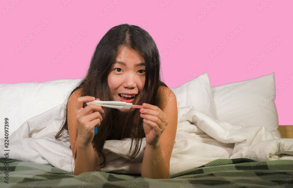 young happy and excited Asian Korean woman in bed holding pregnancy test checking surprised positive pregnant result smiling ecstatic and joyful expecting baby young happy and excited Asian Korean woman in bed holding pregnancy test checking surprised positive pregnant result smiling ecstatic and joyful expecting baby