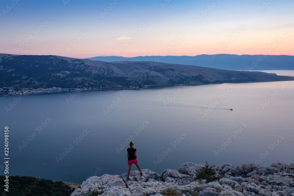 Young woman standing at rock, looking to sunrise and sea