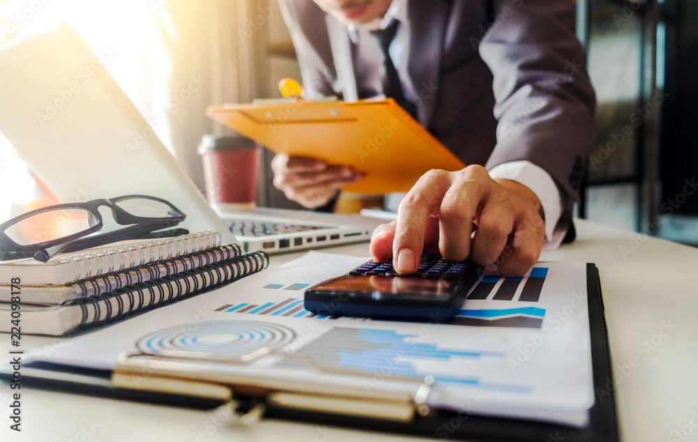 Fototapeta premium Businessman calculates financials with graph paper on the table on the cost of home office in the evening.