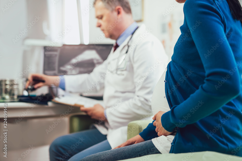 Portrait of male doctor holding document while sitting with pregnant woman in clinic Portrait of male doctor holding document while sitting with pregnant woman in clinic