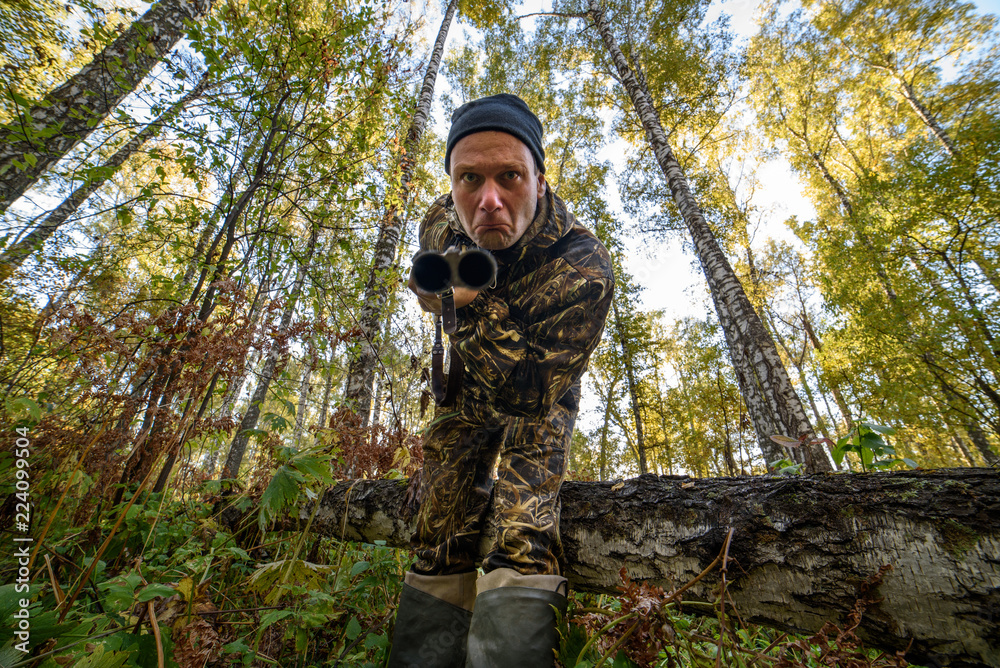 Hunter with a gun in the autumn forest against a background of trees with yellow foliage
