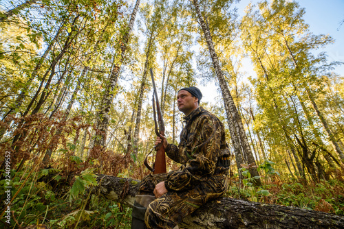 Hunter with a gun in the autumn forest against a background of trees with yellow foliage 