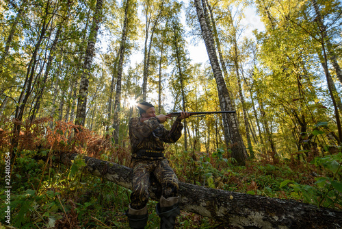 Hunter with a gun in the autumn forest against a background of trees with yellow foliage
