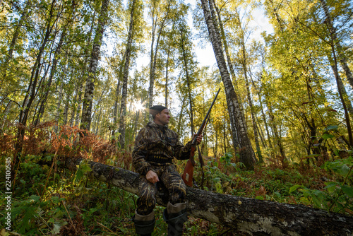 Hunter with a gun in the autumn forest against a background of trees with yellow foliage 