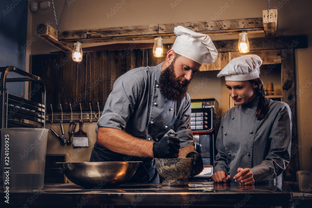Chef grinds sesame seeds in a mortar for cooking bread. Chef teaching his assistant to bake the bread in bakery. Chef grinds sesame seeds in a mortar for cooking bread. Chef teaching his assistant to bake the bread in bakery.