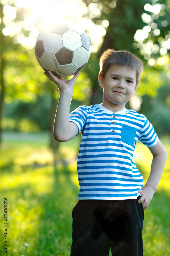 Portrait of a cute little boy with football sitting on grass in the park Portrait of a cute little boy with football sitting on grass in the park