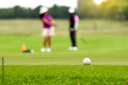 White Golf ball on tee ready to be shot on blurred beautiful landscape of golf course in bright day time with golfer playing golf on course. Sport, Recreation, Relax in holiday concept.